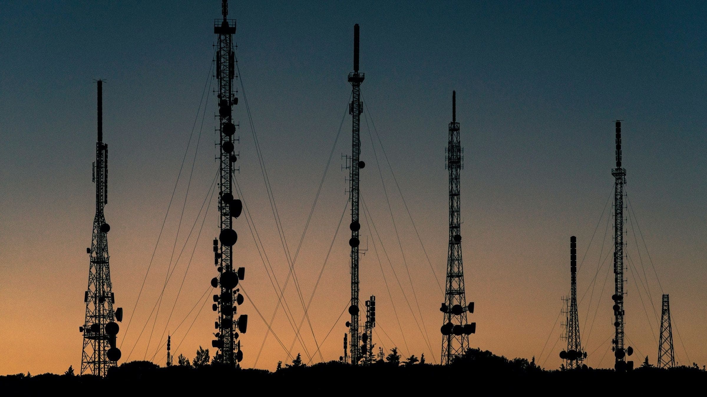 Telecommunication towers silhouetted against an amber dusk